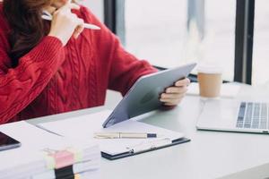 Young business woman sitting in office at table and using smartphone. On desk is laptop and tablet computer, on screen charts and graphs. Woman analyzing data. Student learning online. photo