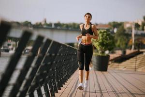 hermosa mujer joven activa corriendo en el paseo marítimo a lo largo de la orilla del río foto