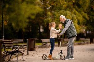 un anciano enseñando a su nieta a andar en patinete en el parque foto