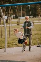 Grandfather spending time with his granddaughter in park playground on autumn day photo