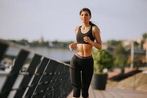 hermosa mujer joven activa corriendo en el paseo marítimo a lo largo de la orilla del río foto