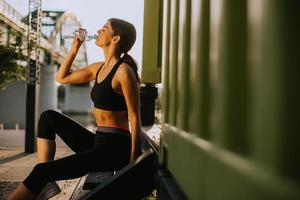 mujer joven y guapa tomando un descanso durante el ejercicio al aire libre y bebiendo agua foto
