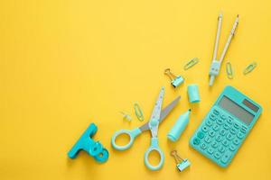 Blue stationery items on the yellow background with free space for text. Creative, colorful background with school supplies. Flatlay with copy space, top view. Marker, pen, paper clips, scissors. photo