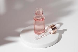 botella de vidrio rosa de gel transparente líquido cosmético sobre fondo blanco. frasco cuentagotas, ácido hialurónico, aceite, suero, producto para el cuidado de la piel. foto