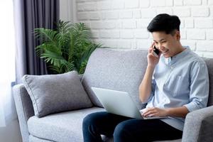 los jóvenes asiáticos están satisfechos con su éxito a través de la comunicación mediante un teléfono inteligente que funciona en casa. tecnología de concepto foto