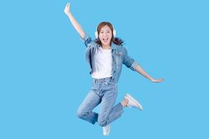 Beautiful Asian woman is smiling happily while listening to music and jumping. On a blue background in the studio. photo