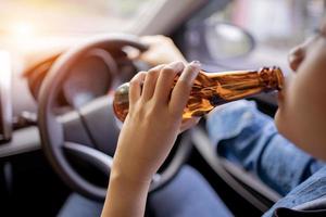 Asian woman drinking beer while driving in dangerous city sunset, right-hand drive system. photo