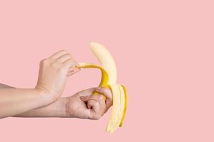 Young woman's hands peeling a yellow banana on pastel yellow background. photo