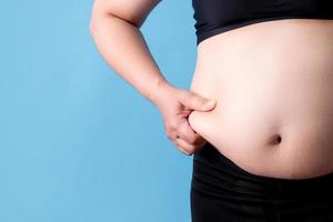 Overweight woman catches fat on her belly on a blue background. Isolated background photo