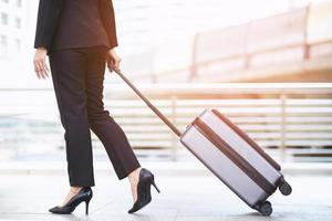 mujer de negocios caminando fuera del edificio de transporte público con equipaje en hora punta. viajero de negocios tirando de la maleta en la moderna terminal del aeropuerto. viaje de negocios de equipaje. foto