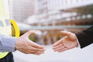 Handsome construction workers in protective helmets and vests are shaking hands while working in the office center photo