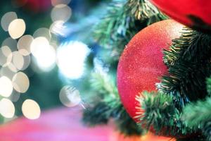 Closeup of red bauble hanging from a decorated christmas tree on blurred of  lights with decorated tree, sparkling and bokeh background. copy space for your text. photo