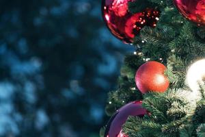 Closeup of red bauble hanging from a decorated christmas tree on blurred of  lights with decorated tree, sparkling and bokeh background. copy space for your text. photo