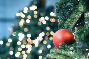 Closeup of red bauble hanging from a decorated christmas tree on blurred of  lights with decorated tree, sparkling and bokeh background. copy space for your text. photo