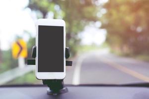 cierre la mano sosteniendo usando un teléfono inteligente móvil con pantalla negra en la consola del automóvil palo del soporte del parabrisas delantero. inserte el mapa de viaje de navegación gps en el fondo del tablero. copie el espacio. foto