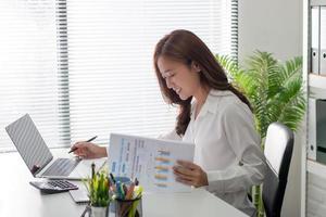 A side view of an asian businesswoman working on a white desk in the office. photo