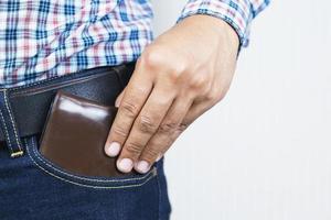 cierra a un hombre confiado posando en una caja fuerte guardando el dinero de tu billetera en el bolsillo delantero de sus pantalones vaqueros de bolsillo delantero. fondo papel pintado blanco foto