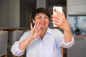 mujer mayor feliz agitando su mano en el teléfono como si tuviera una videollamada con sus amigos, hijos, nietos, etc. uso de tecnologías modernas. enfoque selectivo en el teléfono foto