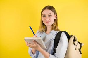 Closeup of a happy caucasian female taking notes in copybook on yellow studio background. Prepare checklist of school or college photo