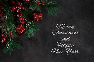 Top view on fir tree branches and gift boxes on dark background. Banner with merry christmas and happy new year text photo