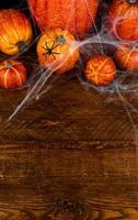 Top view on pile of pumpkins cover in web and spiders.Spooky halloween background.Vertical Flat lay on wooden background with place for text photo