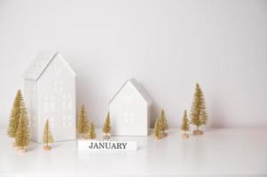 Winter banner with toy houses,christmas trees and january block in white and golden colors. photo