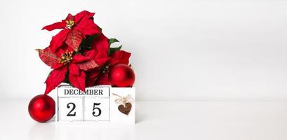 calendario de madera blanca cerca de adornos navideños y poinsettia. banner de vacaciones con lugar para texto foto