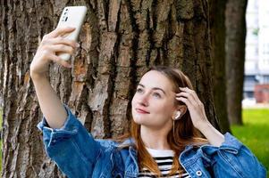 Red haired smiling girl taking selfie while listening to music.Leisure in the park.Use of technologies photo