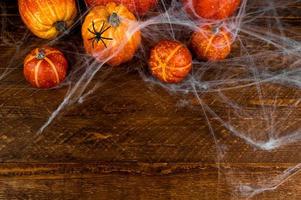 Top view on pile of pumpkins cover in web and spiders.Spooky halloween background.Flat lay on wooden background with place for text photo