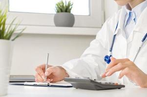 Medical insurance concept . side view on Unrecognizable doctor or nurse with calculator at the table with stethoscope and forms photo