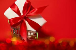 a huge gift with a red ribbon in a shopping cart with some bokeh. Place for text. Mockup photo