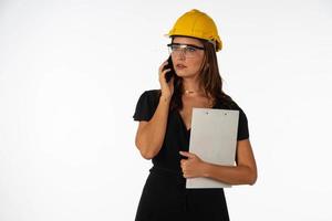 Young beautiful woman engineer holding mobile phone and folder  on isolated white background photo