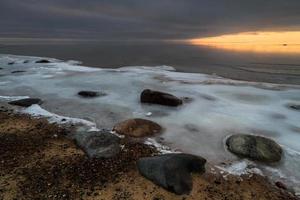 costa del mar báltico con guijarros y hielo al atardecer foto