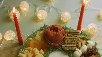 charcutería plana con salami, diferentes tipos de queso. tiene frutos secos, frutos secos varios y miel. arreglo de vacaciones con velas encendidas video