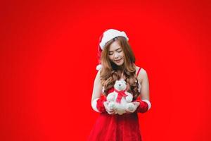 Asian teenage girl dressed as Santa Claus and holding a teddy bear Red background. Christmas concept. photo