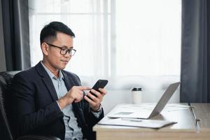 Business man using smartphone after working with laptop on table, man using mobile phone to search or social media or shopping online or stock or crypto currency. Smart phone conversation conferrence. photo