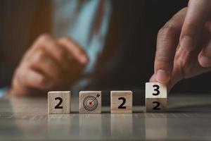 Businessman sitting behide the wooden dices with happy new year changing number 2022 to 2023 goal on wood table. Happy new year change from something new or change from something old to something new. photo