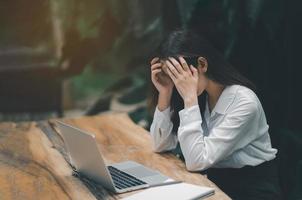 Asian freelance woman hand over head having stressful depression sad time while working on laptop at home. Depression woman sad serios working from home. Working at anywhere concept. photo