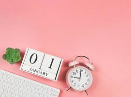 flat lay of computer keyboard, wooden calendar 01 January, pink vintage alarm clock 9 o'clock and succulent plant pot on pink background. First morning of new year. photo