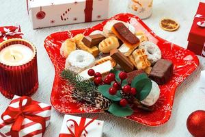 vista superior de turrón dulce de navidad, mantecados y polvorones con adornos navideños en un plato rojo en forma de estrella navideña. surtido de dulces navideños típicos de españa foto