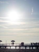 siluetas de personas en el puente a la orilla del mar. la gente ve la puesta de sol. costa del mar muelle en el mar. foto