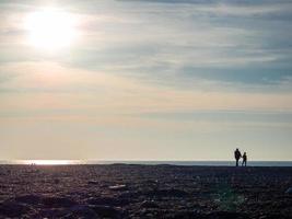 Father and son on a spring pebble beach at sunset. Silhouettes of people on the shore. Vacation on the beach. Rest on the sea. Rocky shore. photo