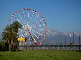 rueda de la fortuna con el telón de fondo de montañas y palmeras. costa de la ciudad sureña. parque de atracciones y montañas. foto