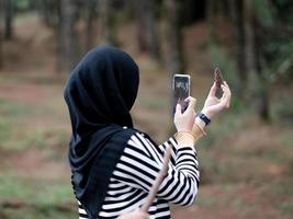 A woman in hijab taking photo with a smartphone