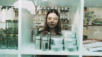 une jeune commerçante caucasienne travaille en organisant des produits réutilisables dans les vitrines d'un magasin de recharge, zéro déchet, des produits d'épicerie sans plastique et un démarrage d'entreprise de vente au détail respectueux de l'environnement. video