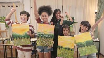 groupe d'artistes dans un studio de classe, un enseignant et des enfants élèves fiers de montrer un travail de peinture, une image en couleur acrylique sur toile, un apprentissage créatif avec des talents à l'école primaire. video