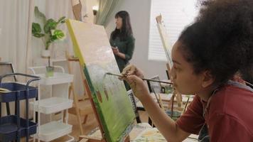 A Black girl concentrates on acrylic color picture painting on canvas with multiracial kids in an art classroom, creative learning with talents and skills in the elementary school studio education. video