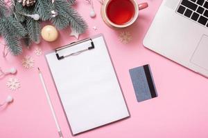 Blank paper on tablet and credit card with Cristmas New Year work table decoration top view, flat lay on pink background photo