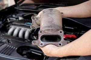 Close up old catalytic converter in hand Technician remove from engine gasoline car dust clogged condition on filter in service concept photo