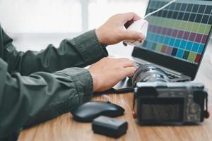 primer plano del fotógrafo manual escribiendo en el teclado del portátil para ajustar el programa en la calibración de la pantalla y la batería de la cámara en la mesa de madera foto